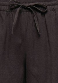 Zbliżenie na ciemnobrązowe spodnie z elastycznym pasem i wiązanym sznurkiem z przodu.