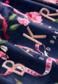 Navy fabric with floral patterns in pink and green, featuring gold embroidered text that reads "BAKER" and decorative ribbons.