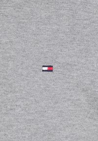 Vaaleanharmaa villapaita, jossa on sileä pinta; edessä pieni sininen, valkoinen ja punainen brodeerattu logo.