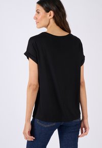 Zwart T-shirt met korte mouwen en opgerolde manchetten, ronde halslijn en een ontspannen pasvorm, gedragen met donkerblauwe jeans, gezien vanuit de achterkant.