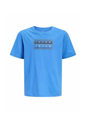 Jongen met kort donker haar staat en draagt een grijze capuchontrui met rits, een blauw t-shirt, zwarte broek en zwarte sneakers, kijkt iets opzij.