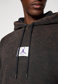 Close-up of a person wearing a black and brown marbled hoodie with a purple Jumpman logo and "Flight" text on the chest.