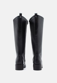 Bottes montantes en cuir noir avec un design droit, fermetures éclair au dos, et un bout rond avec une semelle texturée pour l'adhérence.