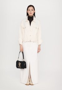 Jaqueta de ganga branca com botões prateados sobre um suéter de gola alta preto, combinada com uma saia maxi branca e ténis bege. Bolsa preta com o logotipo "LOVE".