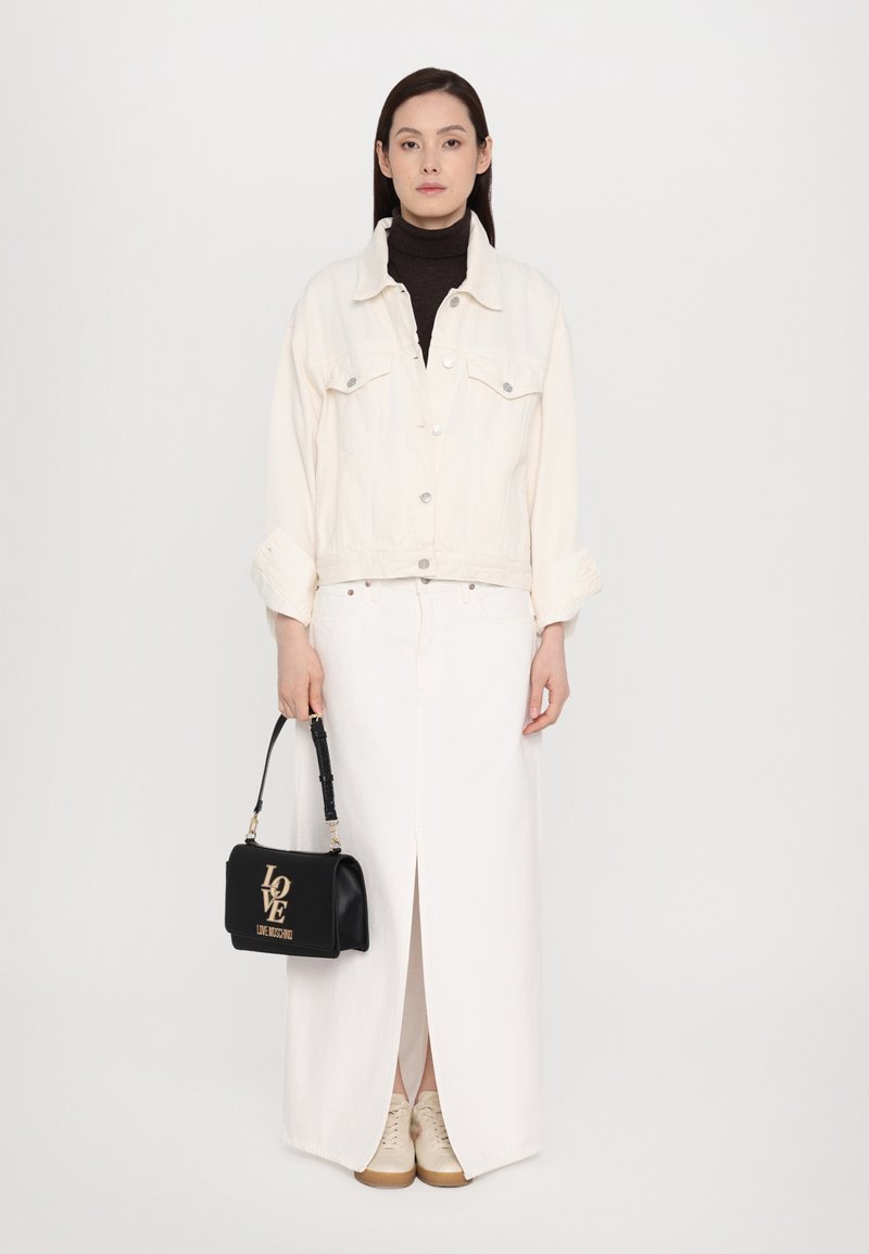 Jaqueta de ganga branca com botões prateados sobre um suéter de gola alta preto, combinada com uma saia maxi branca e ténis bege. Bolsa preta com o logotipo "LOVE".