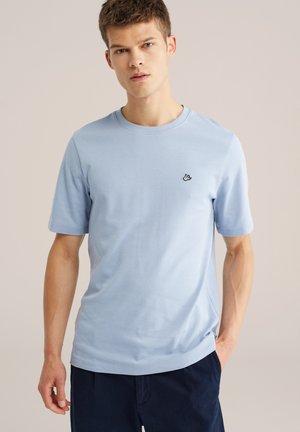 Lichtblauw katoenen T-shirt met korte mouwen, ronde hals en een klein zwart vogellogo op de borst. Eenvoudige, gladde textuur.