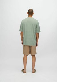 Camiseta verde de manga corta con corte recto, combinada con pantalones cortos beige. La tela parece suave y ligera, adecuada para un uso casual.