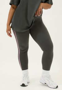 Grå leggings med rosa sidostripes, åtsittande design och stretchigt material. Kombinerat med vita sneakers och en lösgrå topp.