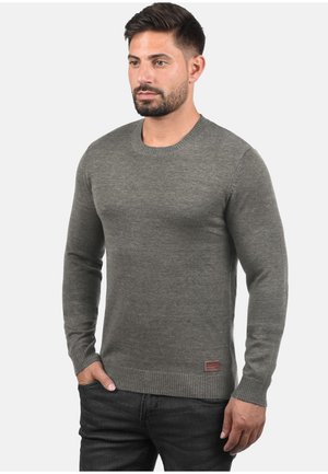 Grijze gebreide trui met lange mouwen, ronde hals en ribgebreide manchetten. Heeft een klein logo-patch nabij de zoom. Glad textuur.
