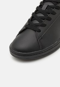 Sneaker in pelle nera con una texture liscia, punta arrotondata, lacci neri e suola in gomma con dettagli di cucitura sottili.
