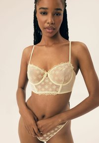 Koronkowy biustonosz w delikatnym żółtym kolorze z kwiatowym haftem, z wsparciem drucianym, regulowanymi ramiączkami oraz pasującymi przezroczystymi majtkami z detalami.