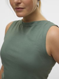 Close-up of person wearing sleeveless light green top and silver twisted drop earring, with lips slightly smiling.