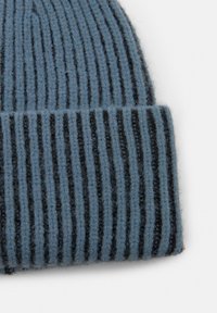 Kék-szürke színű kötött sapka, váltakozó fekete csíkokkal, puha, texturált anyagból készült, hajtott résszel.