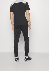 Conjunto atlético negro que incluye una camiseta de mangas cortas y pantalones ajustados, con acentos grises en los hombros y las costuras laterales. Tejido sintético texturizado.