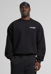 Black sweatshirt with a crew neckline, ribbed cuffs, and a subtle white "KARL KANI" logo on the chest. Soft fabric texture with a relaxed fit.