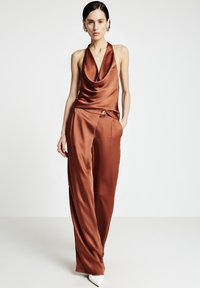 Satin-Halfter-Top in Rostfarbe mit drapiertem Ausschnitt, kombiniert mit weitem Hosenbein, das eine Seitentasche und dekorative Knopfdetails aufweist.