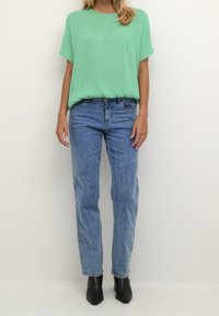 Lys grøn kortærmet bluse parret med højtaljede blå jeans og sorte ankelstøvler. Blusen har en løs pasform og en blød tekstur.