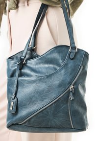 Sac fourre-tout en cuir bleu avec un design courbé, doté d'une poche zippée et d'un motif perforé, complété par des doubles poignées.