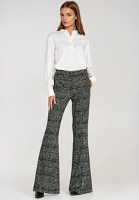 Biała bluzka z długim rękawem i częściowym rozpięciem na guziki, zestawiona z wysokim stanem, rozszerzanymi spodnimi w czarno-biały wzór.