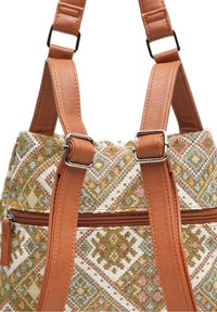 Tkaná textilní taška s geometrickými vzory v zlaté, bílé a pastelových barvách. Hnědé umělé kožené popruhy se stříbrnými kovovými prvky. Detail s kapsou na zip.