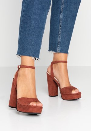 Sandales à talons hauts en daim marron avec semelle plateforme, bout ouvert et bride à la cheville ; dotées d'un talon épais et d'une texture lisse.