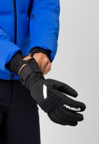 Gants isolés noirs avec une finition texturée, dotés d'accents blancs et d'un poignet ajusté, portés sur une veste bleue. Idéal pour les temps froids.