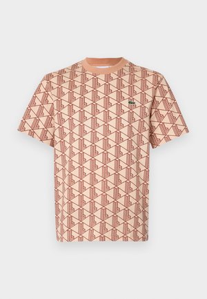 T-shirt a maniche corte realizzata in un tessuto morbido, con una base pesca e un motivo geometrico rosso, accompagnata da un piccolo logo verde sul petto.