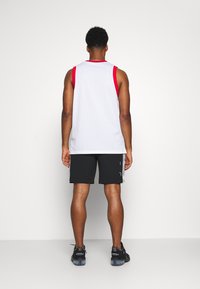 Vit mesh tanktopp med röda accenter, tillsammans med svarta shorts och svarta sneakers. Shorts har sid sömmar med kontrasterande detaljer.