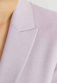 Bordowy żakiet z teksturowanej tkaniny, z wyrazistymi klapami i dopracowanym fasonem. Zbliżenie podkreśla kolor i szczegóły materiału.