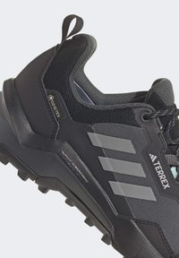 Sorte tursko med nettingsoverdel, forsterket tå, tre grå striper, Gore-Tex-merke og en teksturert gummisåle for grep.