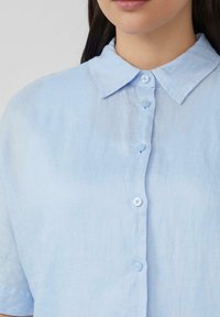 Lichtblauw, kortärmige shirt van een zachte, gestructureerde stof. Beschikt over een klassieke kraag en vijf knopen aan de voorkant.