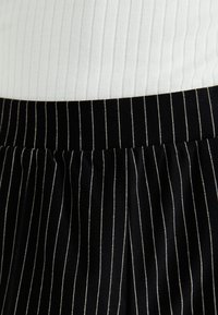 Black pleated skirt with white pinstripes, featuring an elastic waistband and soft texture, paired with a ribbed white top.