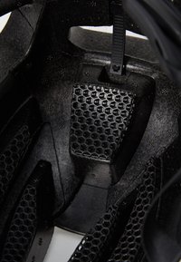 Nahaufnahme des Innenraums eines schwarzen Helms mit einem strukturierten Wabenmuster und verstellbaren Riemen, wobei ein leichtes, atmungsaktives Design betont wird.