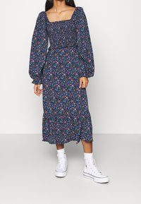 Gaun dengan cetakan bunga, memiliki leher kotak, lengan puff, dan pinggang yang pas, serta dilengkapi dengan rok melebar dan palet warna biru, pink, dan hijau.