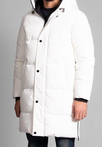 Witte pufferjas met een capuchon, voorzien van een gestikt ontwerp, zwarte knopen en rits zijzakken. Textuurstof met een gladde afwerking.