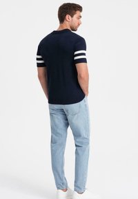 Marinblå polotröja med vita ränder på korta ärmar; matchad med ljusblå jeans och vita sneakers; figurnära design och ribbad halslinning.