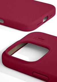 Rød silikondeksel til telefon med en jevn, matte overflate, presise utsparinger for porter og preget tekst med "IDEAL OF SWEDEN" detaljer.