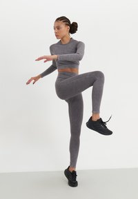 Sivi rebrasti dugi crop top i odgovarajuće tajice s tankim vertikalnim prugama, uparen s crnim sportskim cipelama, model u dinamičnoj pozi.