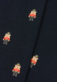 Marinblått stickat tyg med upprepade mönstrade björnar i militärstil, klädda i röda uniformer med guldaccenter och svarta hattar.