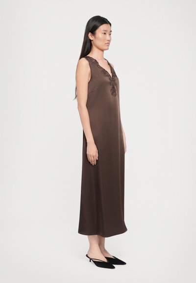 Rochie maro fără mâneci, cu decolteu în V, împodobită cu dantelă și cu o siluetă dreaptă, asortată cu mule negre cu toc. Textura materialului este netedă.