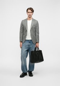 Šedý blazer přes bílé tričko, doplněný o světle modré volné džíny a černé boty. Modelka drží černou koženou tote tašku.