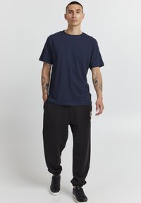 Navyblauwe katoenen t-shirt met korte mouwen, gecombineerd met zwarte sweatpants met een gouden logo accent aan de zijkant. Zwarte sneakers.