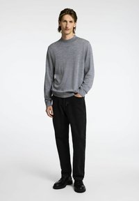 Siv pulover z dolgimi rokavi iz mehkega materiala, v kombinaciji z črnimi kavbojkami in črnimi čevlji. Preprost dizajn, klasične barve.