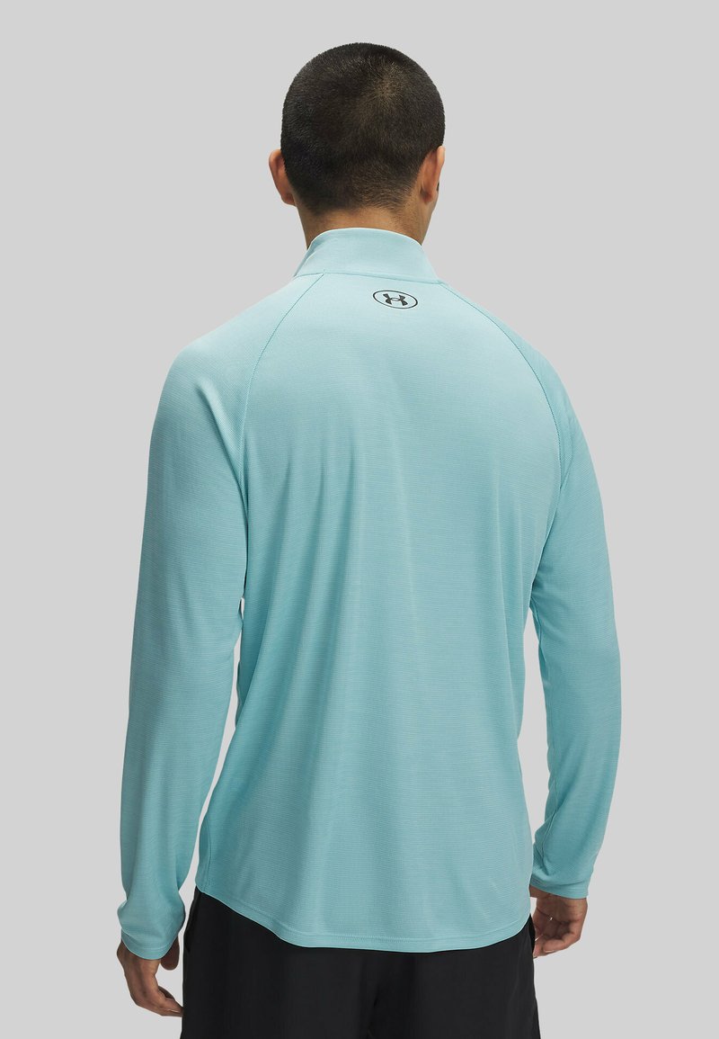 Chemise de sport à manches longues bleu clair avec col, en tissu texturé et détails de logo au dos. Coupe décontractée avec ourlet arrondi.