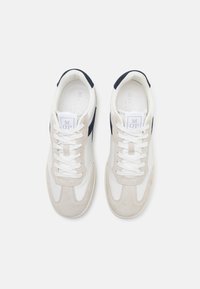Weiße und beige Sneaker mit einem Obermaterial aus Wildleder und Leder, runder Zehenform, kontrastierenden marineblauen Akzenten und weißen Schnürsenkeln. Markenlabel auf der Zunge.