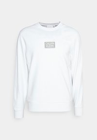 Felpa bianca con maniche lunghe, polsini a costine e scollo rotondo. Presenta un logo quadrato grigio con "CALVIN KLEIN" centrato sul petto.