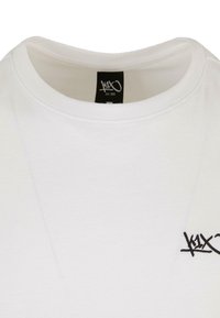 Hvid bomulds T-shirt med rund hals, der har et lille sort logo på venstre bryst. Glat tekstur, klassisk pasform, minimalistisk design.