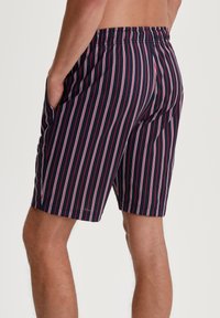 Marineblauwe shorts met verticale witte en rode strepen, elastische tailleband, zijzakken, midden boven de dij en een gladde textuur.