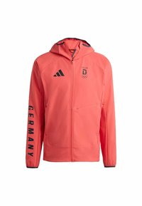 Koraalrode jas met ritssluiting en capuchon, zwarte accenten, "GERMANY" tekst op de mouw en Olympisch logo. Gemaakt van een glad, lichtgewicht materiaal.