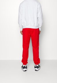 Sudadera gris con puños y dobladillo acanalados, combinada con pantalones deportivos rojos de corte holgado que cuentan con puños elásticos en los tobillos, llevada con zapatillas negras y blancas.